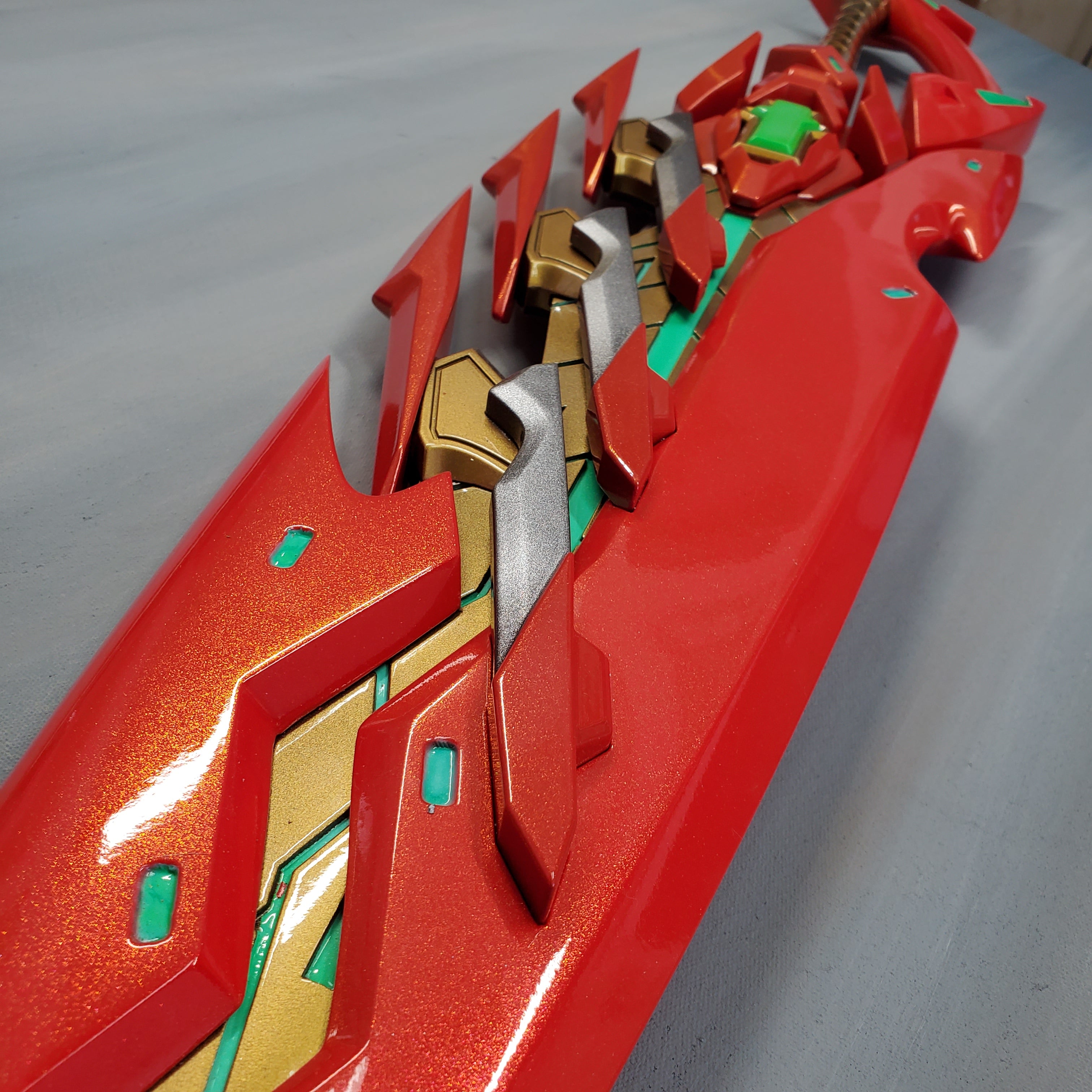 Close-up of a red and gold futuristic weapon on a gray background