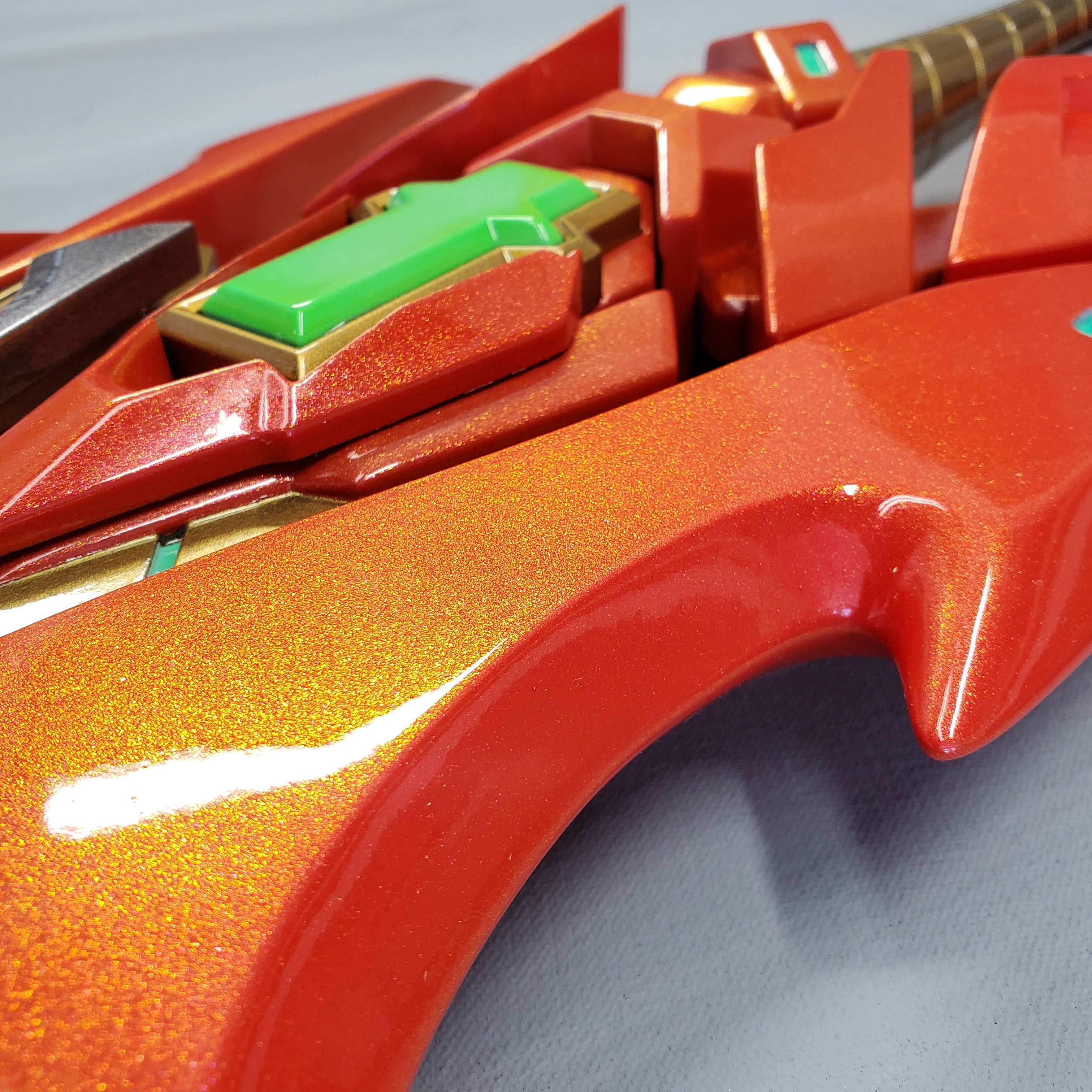 Close-up of a red and gold mechanical object with green accents on a gray background