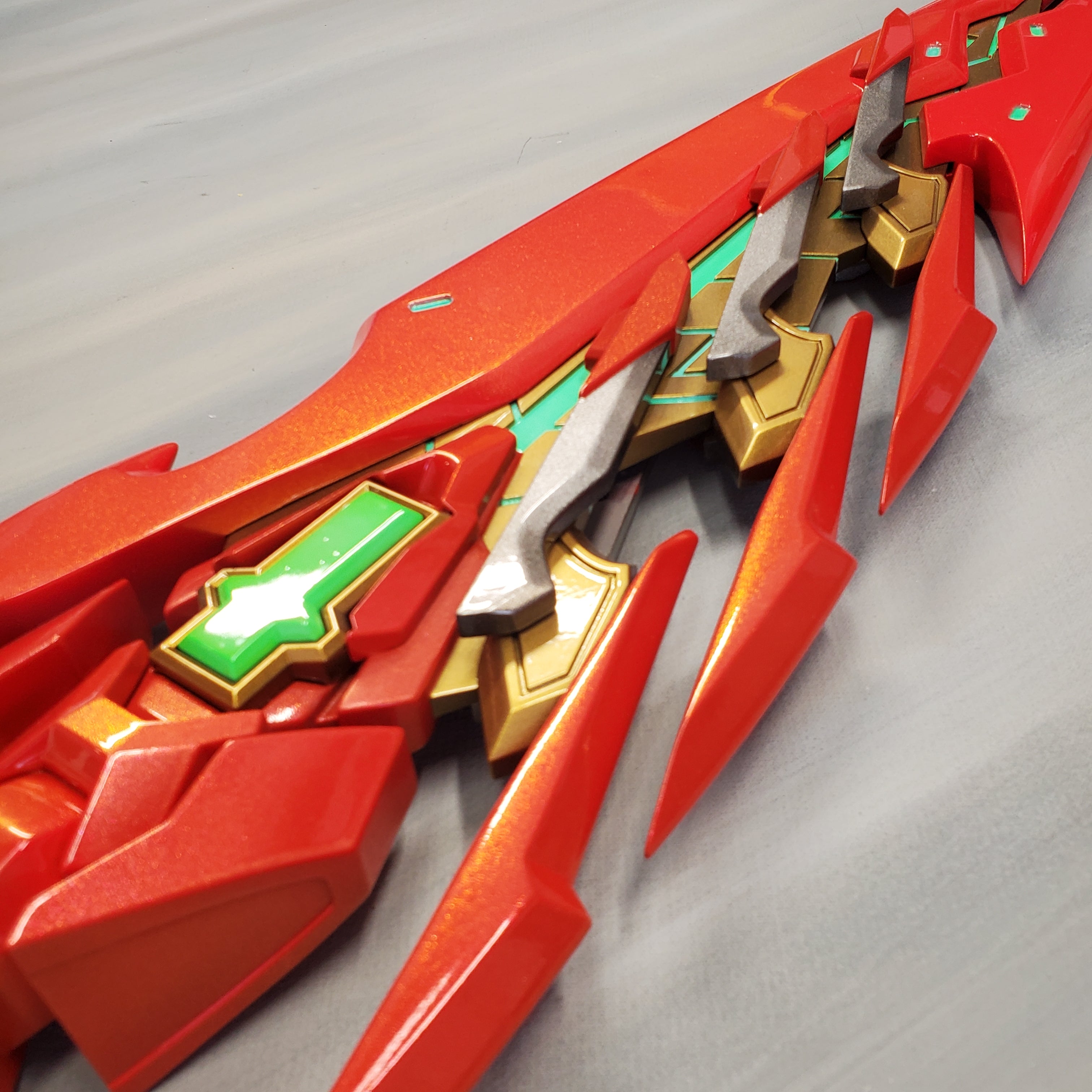 Close-up of a red and gold futuristic weapon on a gray background