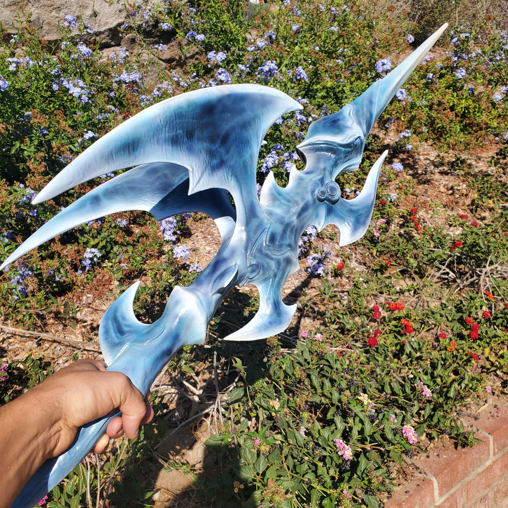 Blue fantasy sword held by a hand in front of a garden with flowers and plants.