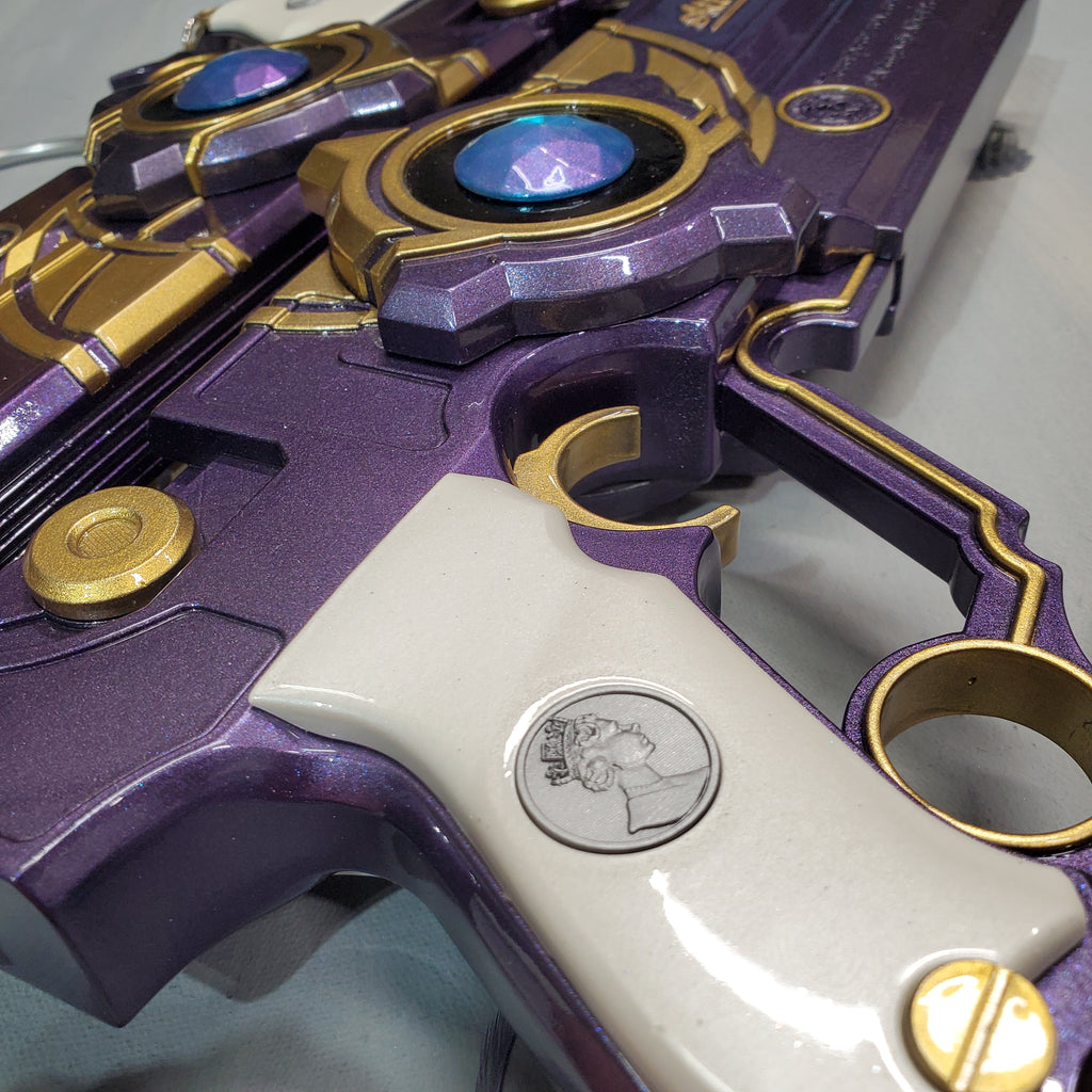 Close-up of a purple and gold toy gun with a white handle.
