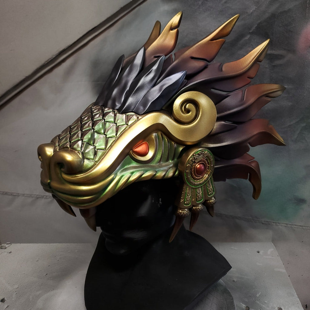 Hand‑sculpted Quetzalcóatl warrior mask with metallic gold, green, and violet detailing displayed on a black mannequin head