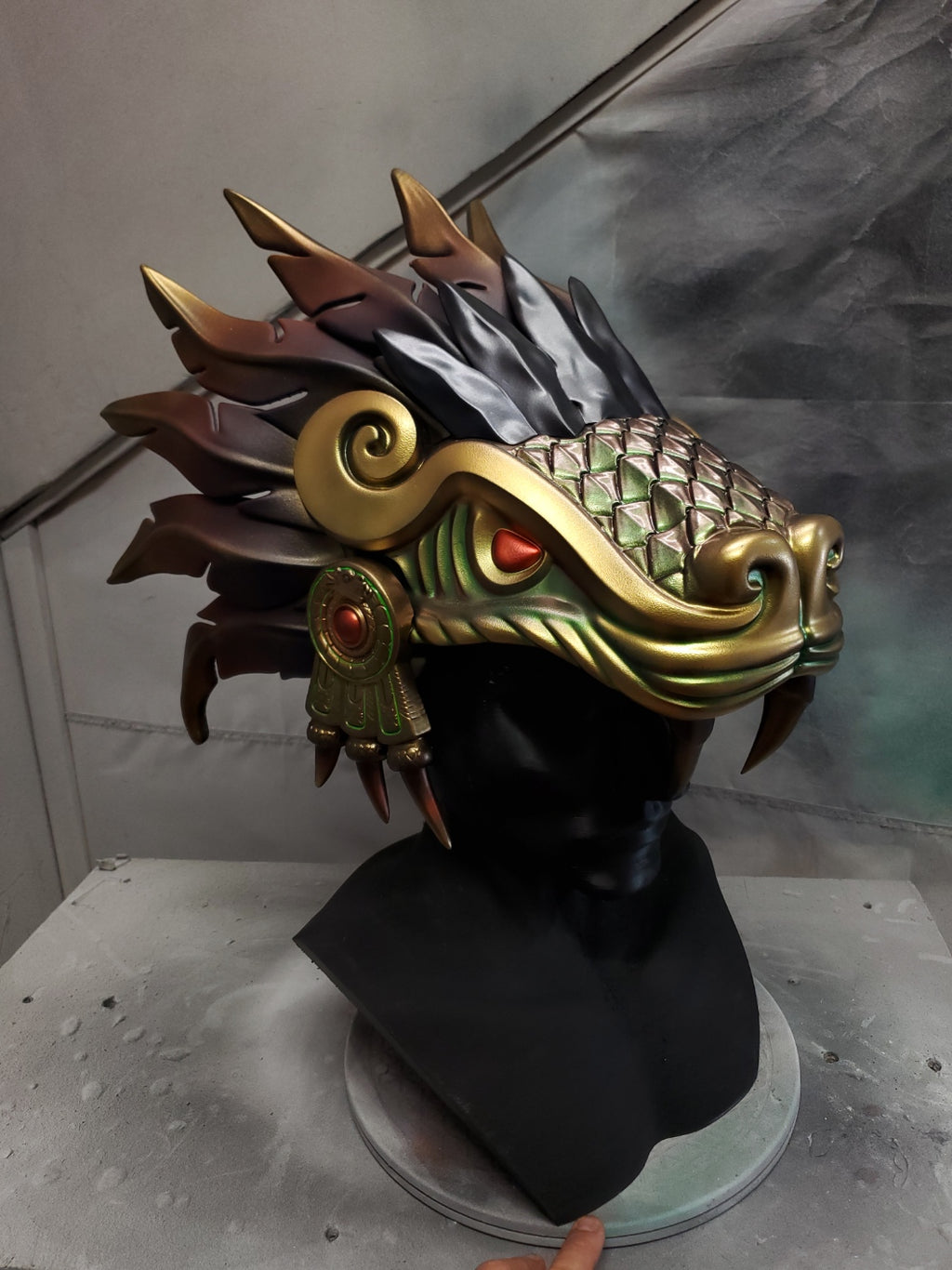 Hand‑sculpted Quetzalcóatl warrior mask with metallic gold, green, and violet detailing displayed on a black mannequin head