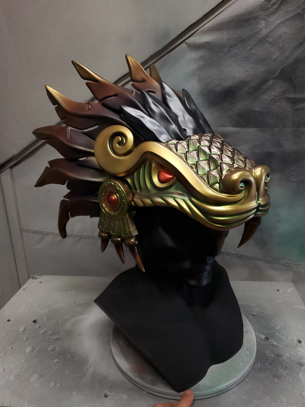 Hand‑sculpted Quetzalcóatl warrior mask with metallic gold, green, and violet detailing displayed on a black mannequin head
