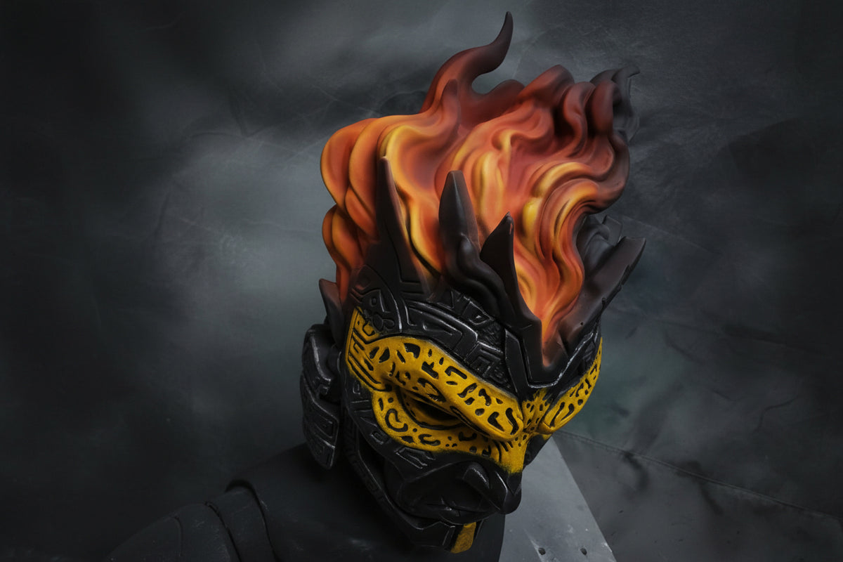 A close-up of a stylized fantasy helmet or mask with black angular armor, a bright yellow patterned lower face, and vivid orange-red flames rising from the top against a dark gray background.