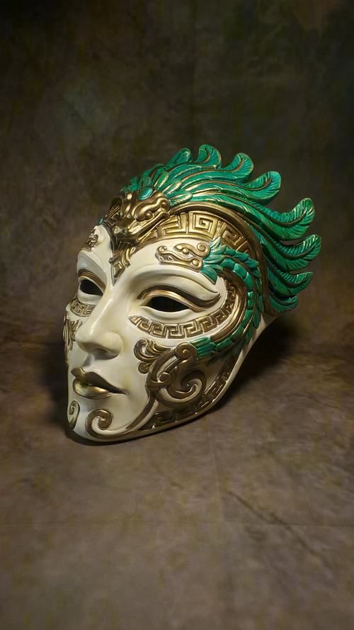 An ornate Venetian-style masquerade mask with a white base, gold filigree detailing, and vibrant green feather-like accents on the top and sides, set against a textured brown background.