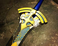 A decorative toy sword with a blue handle and gold, yellow, and silver blade, resting on a dark concrete floor.