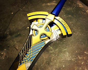 A decorative toy sword with a blue handle and gold, yellow, and silver blade, resting on a dark concrete floor.