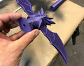 Purple dragon-shaped object held by a hand on a neutral background