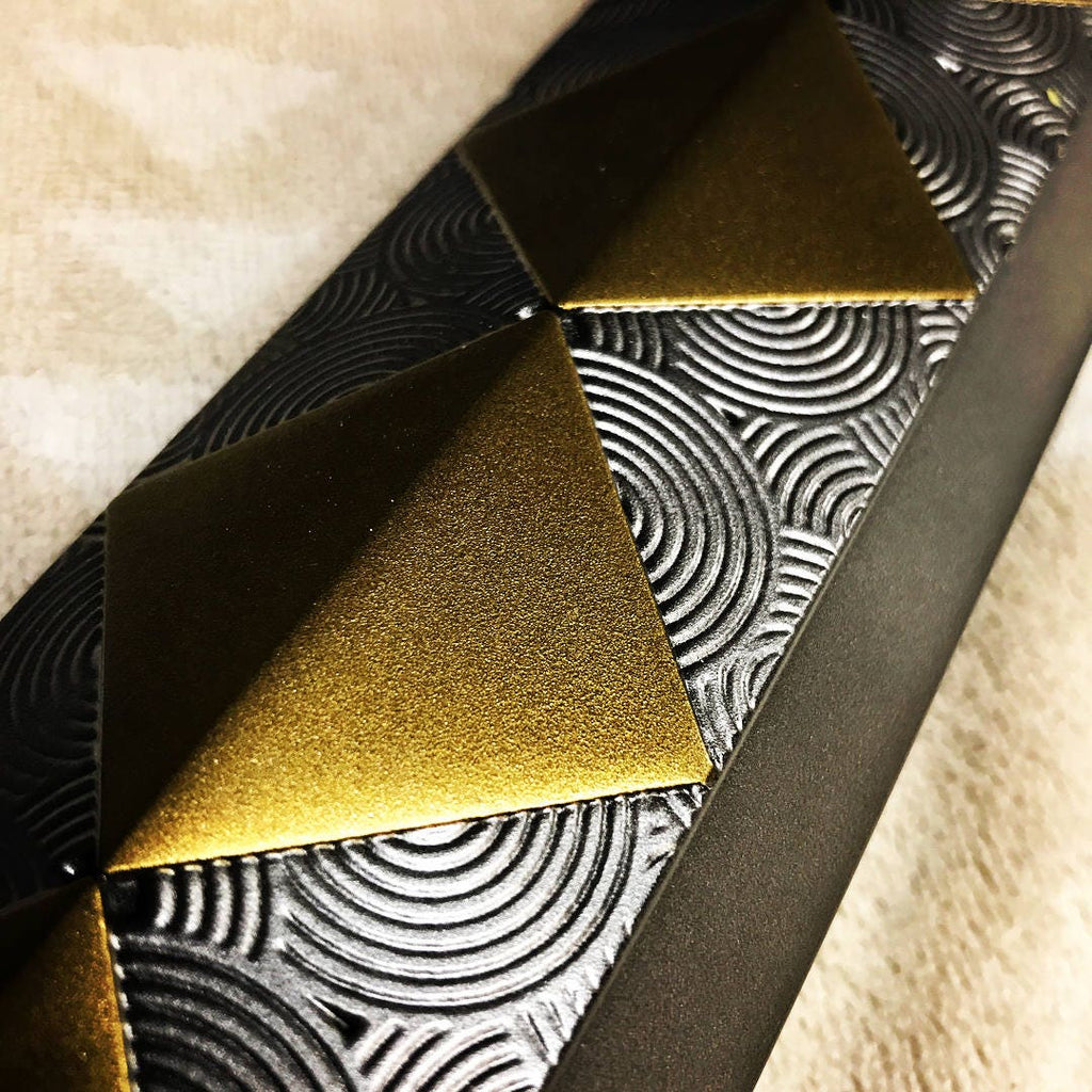 Close-up of a textured black belt with metallic gold pyramid studs and embossed circular patterns.