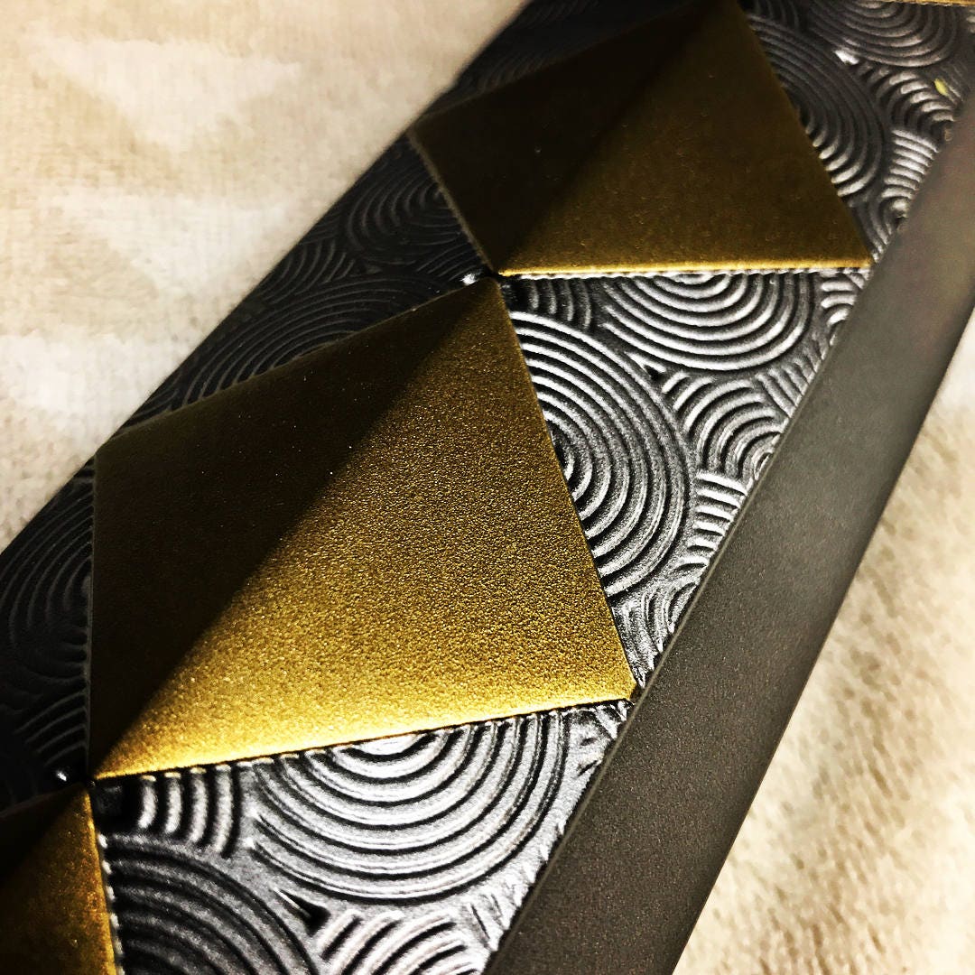 Close-up of a textured black belt with metallic gold pyramid studs and embossed circular patterns.