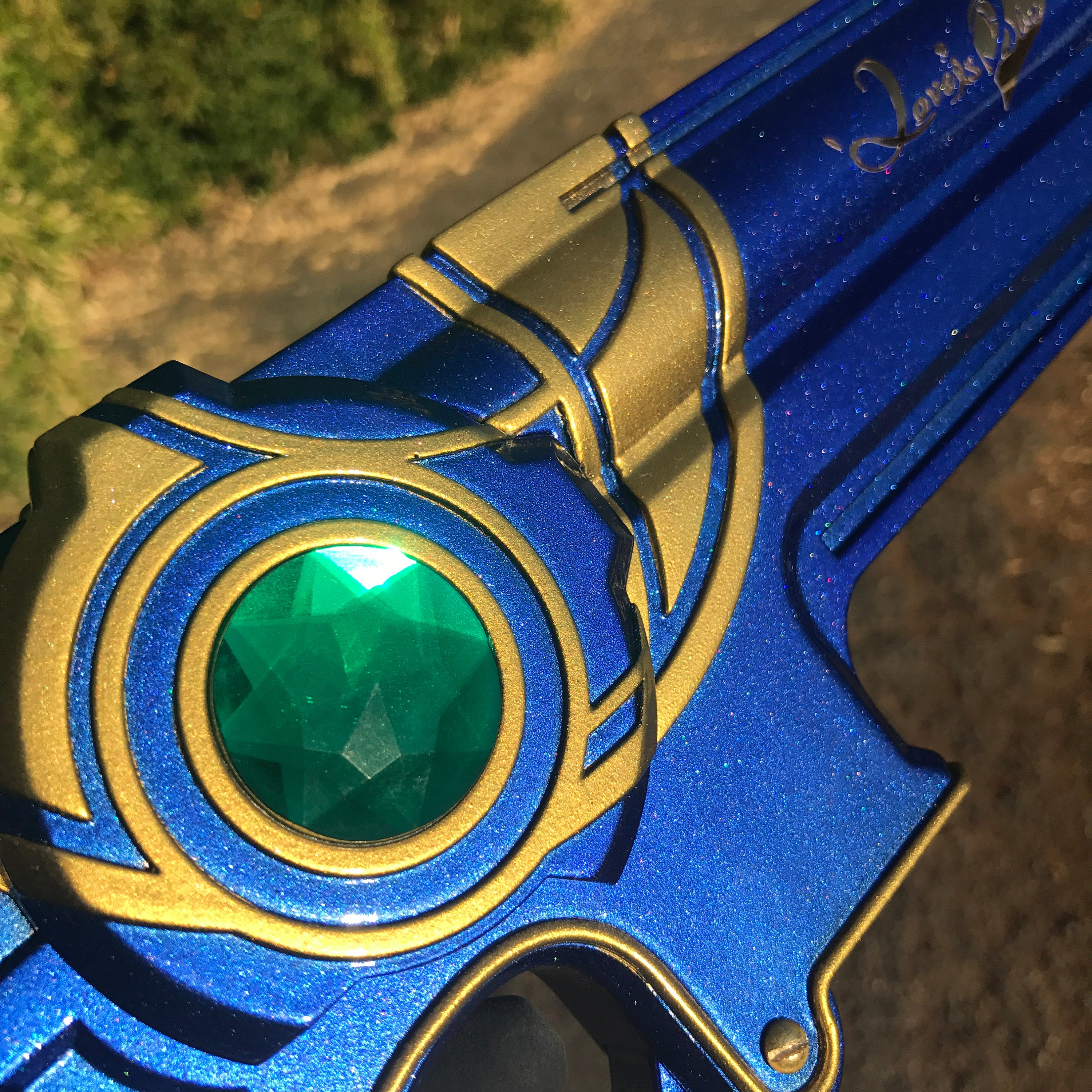 Close-up of a blue and gold object with a green gemstone, outdoors.