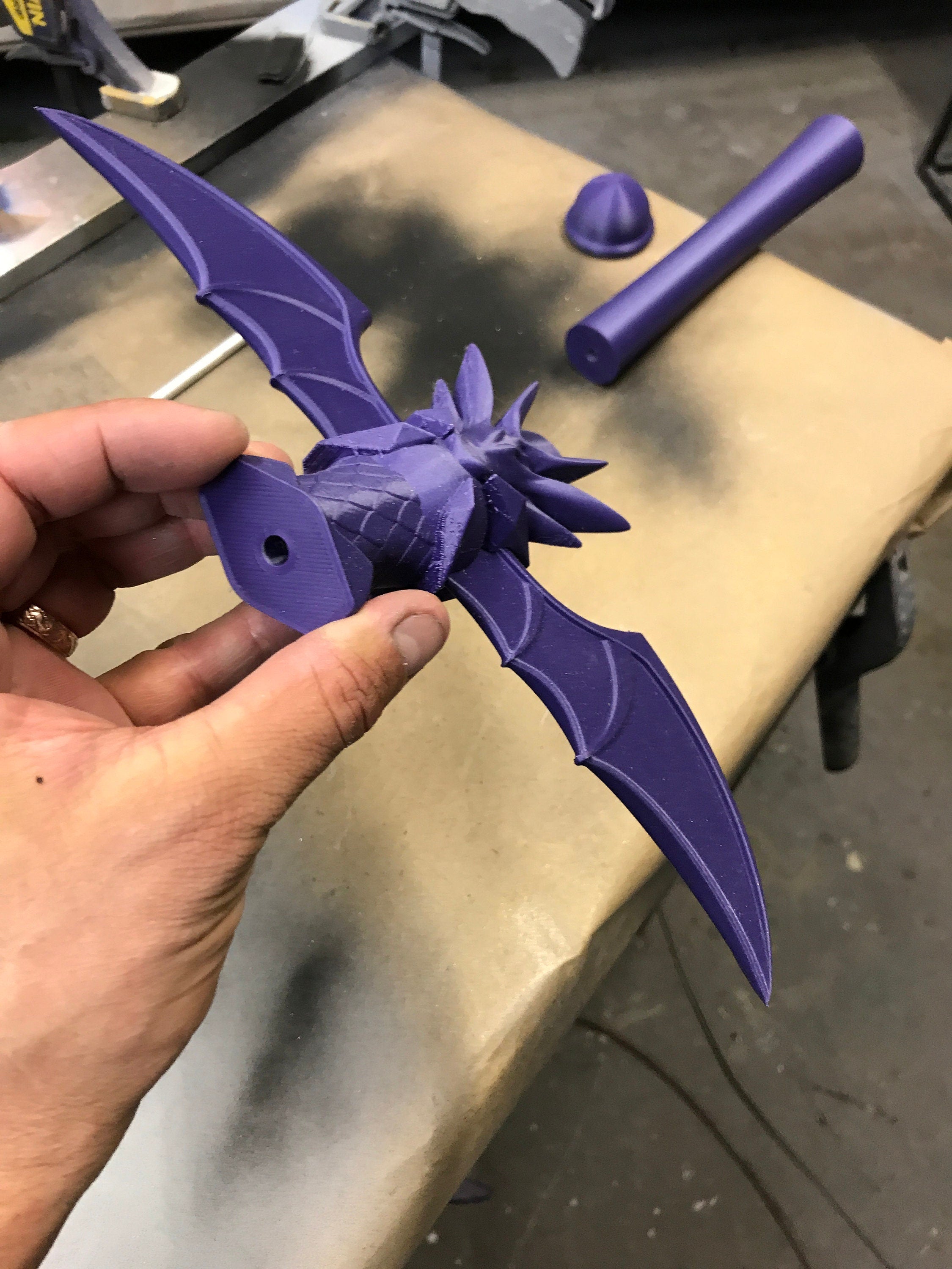 Purple dragon-shaped object held by a hand on a workbench.