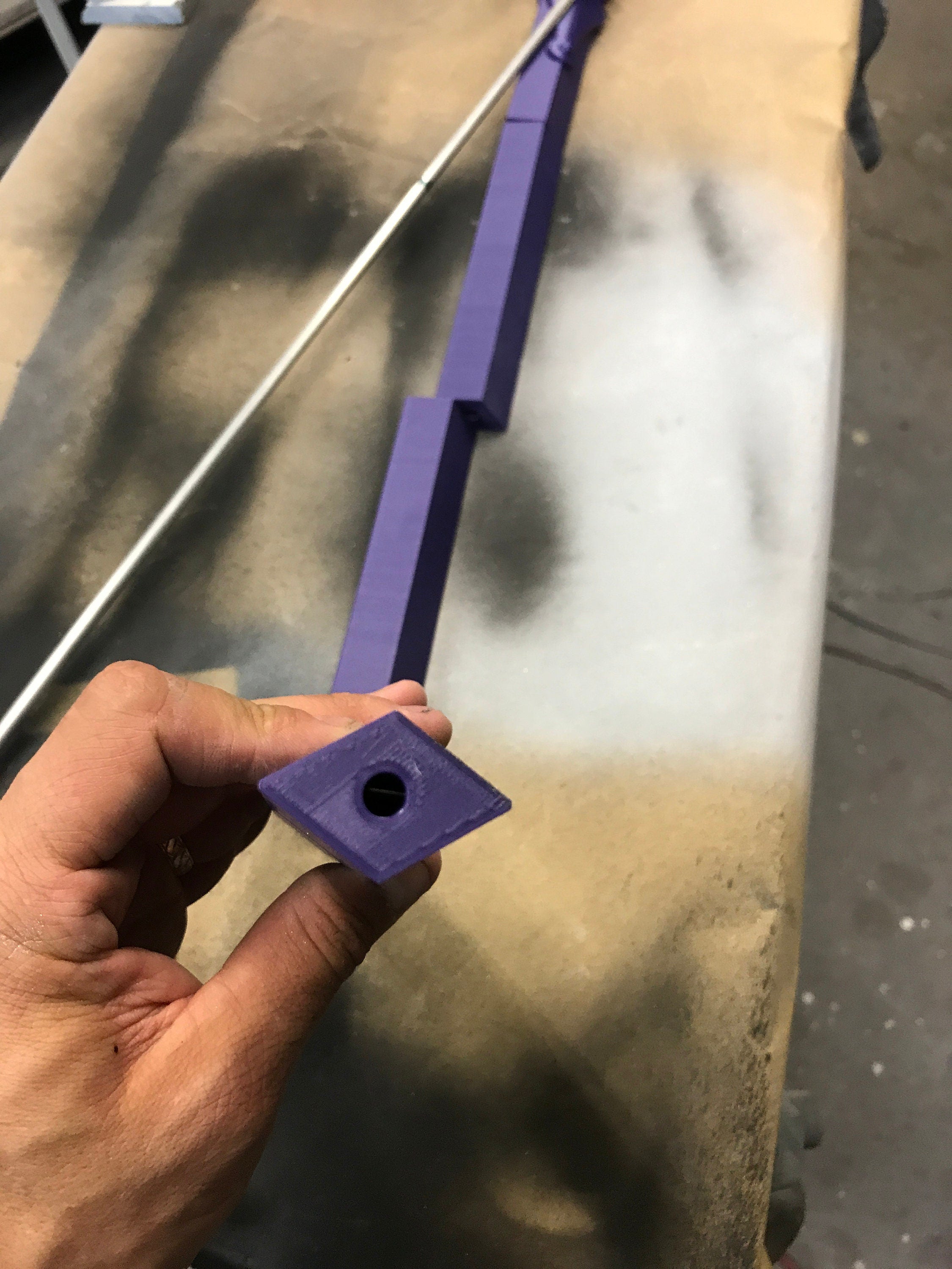 Hand holding a purple square object with a hole against a reflective surface.